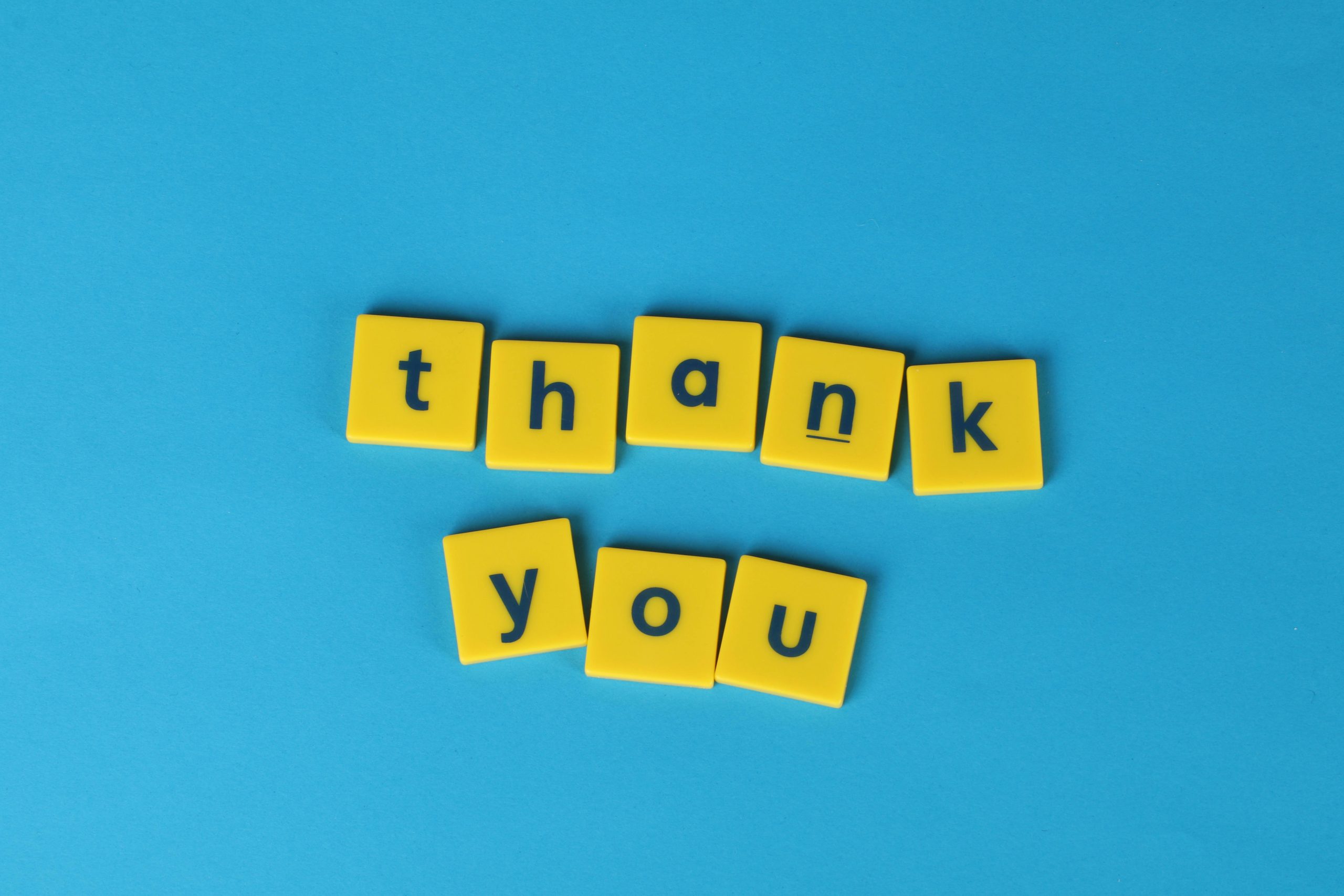 Bright yellow letter tiles spelling 'thank you' on a blue background, perfect for gratitude notes.
